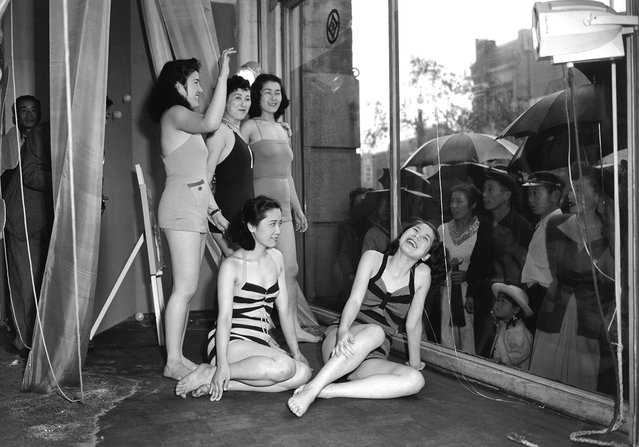 Untuk menarik perhatian publik, sebuah department store di Tokyo menggunakan model-model hidup untuk memamerkan jajaran produk pakaian renang terbaru mereka, 5 Juni 1950. Hujan tidak menghalangi para pejalan kaki yang penasaran tersebut, dan baik para model maupun penontonnya tampaknya menyukai ide saling memandang melalui kaca display tersebut. (Photo by AP Photo via The Atlantic)