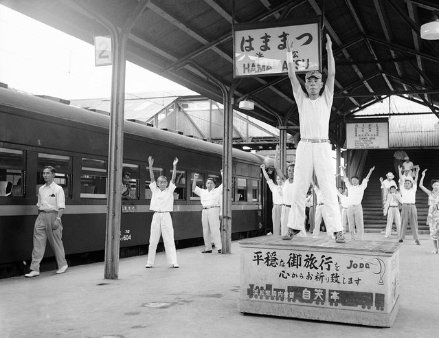 Para penumpang di sebuah kereta api dari Tokyo menuju Osaka tampak mengikuti senam selama tiga menit di bawah bimbingan seorang instruktur, dalam sebuah persinggahan selama lima menit di Hamamatsu, 27 Agustus 1952. Layanan yang tidak biasa ini diadakan untuk membantu para penumpang dalam perjalanan jauh untuk melemaskan otot-otot mereka di stasiun yang merupakan setengah perjalanan diantara Tokyo dan Osaka. Dalam senam ini, disediakan musik untuk senam, dan bahkan sebuah panggung untuk sang instruktur. (Photo by Max Desfor/AP Photo via The Atlantic)