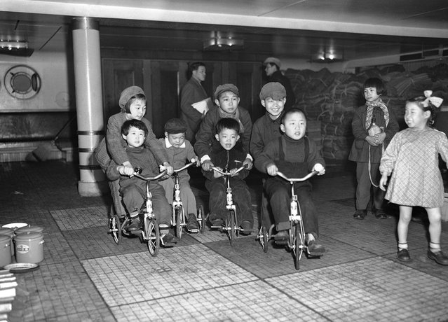 Anak-anak dari keluarga Jepang yang dipulangkan ke negaranya ini bersenang-senang dengan sepedanya di atas dek Kapal Koan Maru selagi orangtua mereka bersiap untuk turun dari kapal di Teluk Maizuru, Jepang, 24 Maret 1953. Kelompok pertama yang dipulangkan dari China dimana mereka terdampar sejak akhir perang dunia kedua ini telah melengkapi formalitas di pusat pemrosesan di Maizuru dan diperbolehkan pulang ke rumah. Gelombang pertama ini terdiri dari 2000 orang pria, wanita dan anak-anak yang datang dari China Utara menaiki kapal Koan Maru ini. Sepeda yang mereka naiki adalah pemberian dari beberapa organisasi amal dan ditempatkan di atas kapal ketika kapal ini meninggalkan China. (Photo by Y. Jackson Ishizaki/AP Photo via The Atlantic)