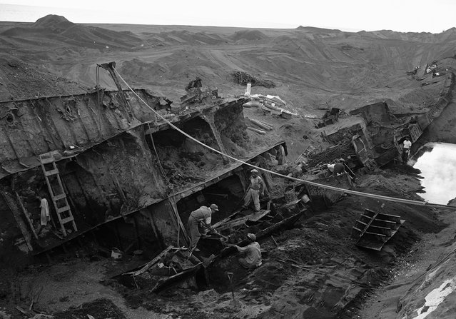 Di pulau Iwo Jima, para pekerja Jepang memotong rongsokan kapal perang yang nyaris terkubur pasir di pantai pada 21 Februari 1954. Setelah sembilan tahun absen, orang Jepang kembali lagi ke pulau Iwo Jima, tapi sebagai pekerja yang bertugas mengambil barang yang bisa diselamatkan. (Photo by AP Photo via The Atlantic)