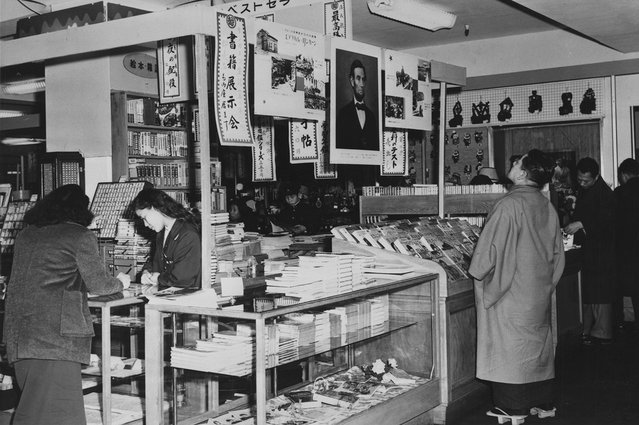 Interior dari sebuah department store di Tokyo pada 1959, dimana seorang pria Jepang mengenakan Geta, sandal kayu tradisional, sedang melihat foto Abraham Lincoln digantung bersama dua poster lain tentang kehidupan Lincoln. (Photo by Library of Congress via The Atlantic)