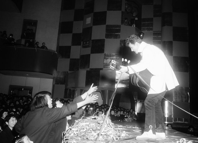 Micky Curtis, seorang penyanyi bergaya mirip Elvis Presley, memainkan gitarnya dan menyanyi, selagi para gadis pemujanya berusaha meraihnya, di Nichigeki Theater di Tokyo pada 18 Februari 1958. Jepang saat itu dilanda demam "Rock'n Roll" sehingga musik barat pun merajai tangga lagu Jepang. (Photo by AP Photo via The Atlantic)