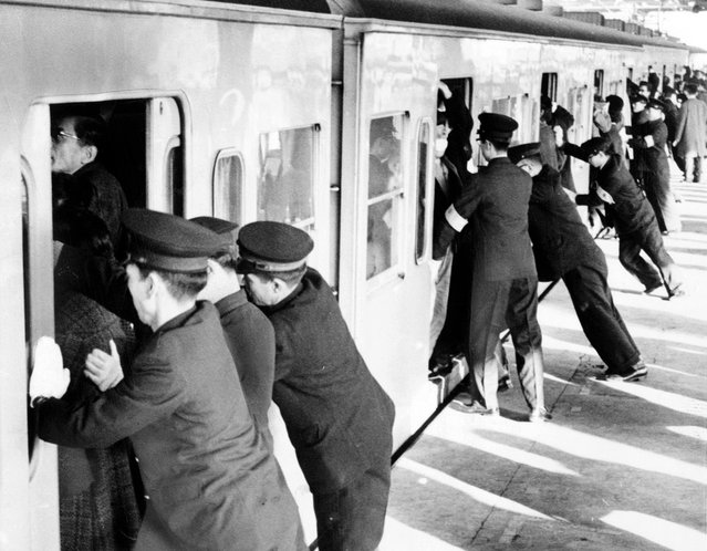 Para mahasiswa yang bekerja sebagai "petugas pendorong" mendesakkan para penumpang ke dalam kereta komuter di Tokyo. (Photo by Library of Congress via The Atlantic)
